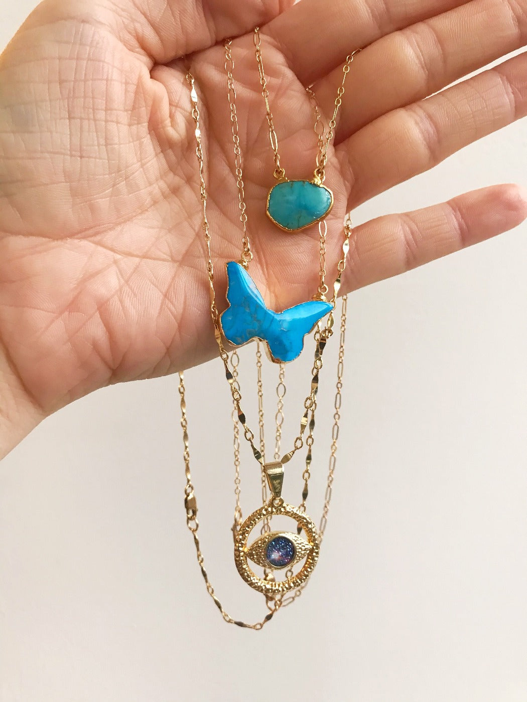 turquoise butterfly necklace layered with turquiose and gold evil eye necklaces